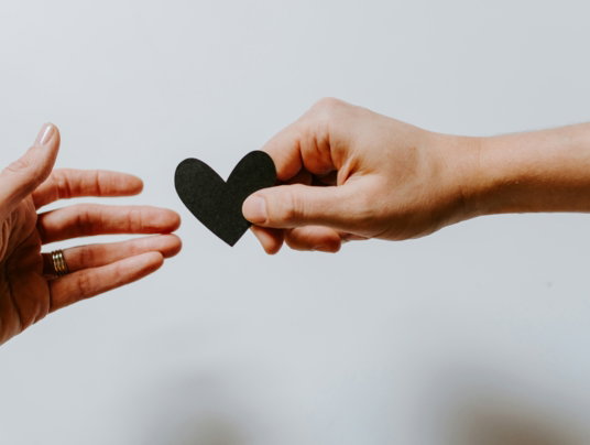 person reaching black heart cutout paper