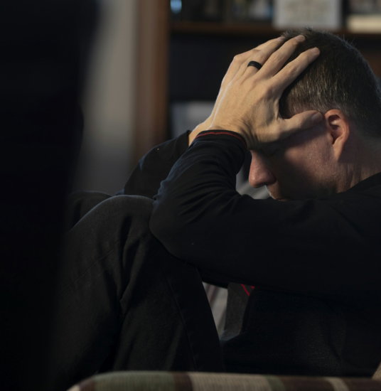 a-man-sitting-on-a-couch-holding-his-head-in-his-hands.jpg a man sitting on a couch holding his head in his hands